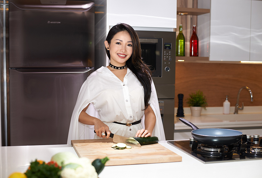 A long haired women with white dress shirt is cooking in the kitchen